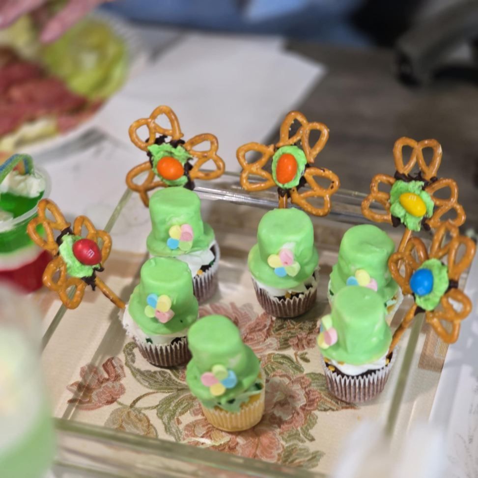 Cupcakes with green frosting and pretzel toppers, on a floral tray, with colorful decorations.
