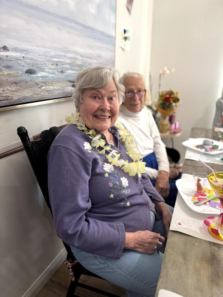 A woman with a white flower lei smiles next to an older man. Coral Tree Care Home in Lomita, CA.