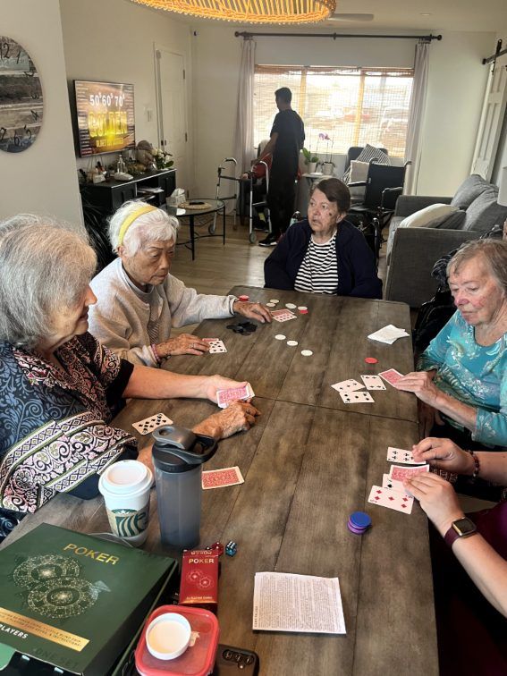 Four older women playing cards around a wooden table. Coral Tree Care Home in Lomita, CA.