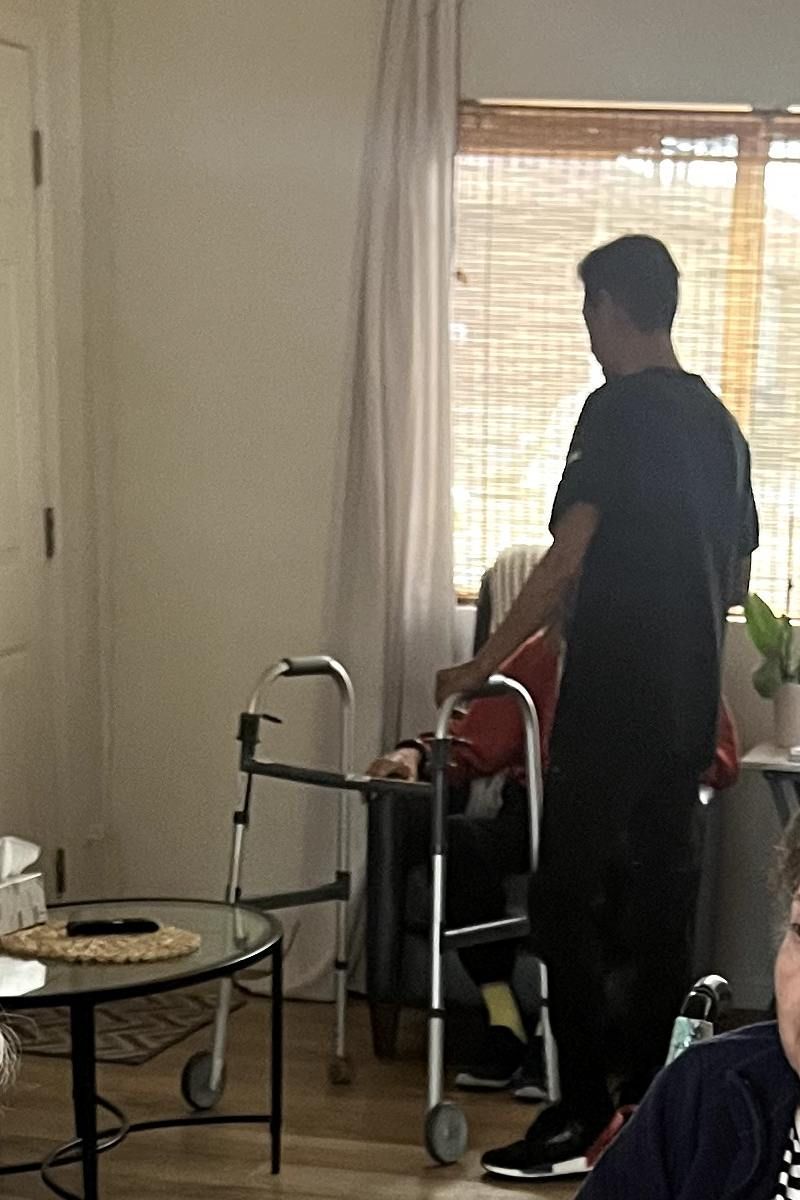 A man assists an elderly person with a walker indoors. Coral Tree Care Home in Lomita, CA.