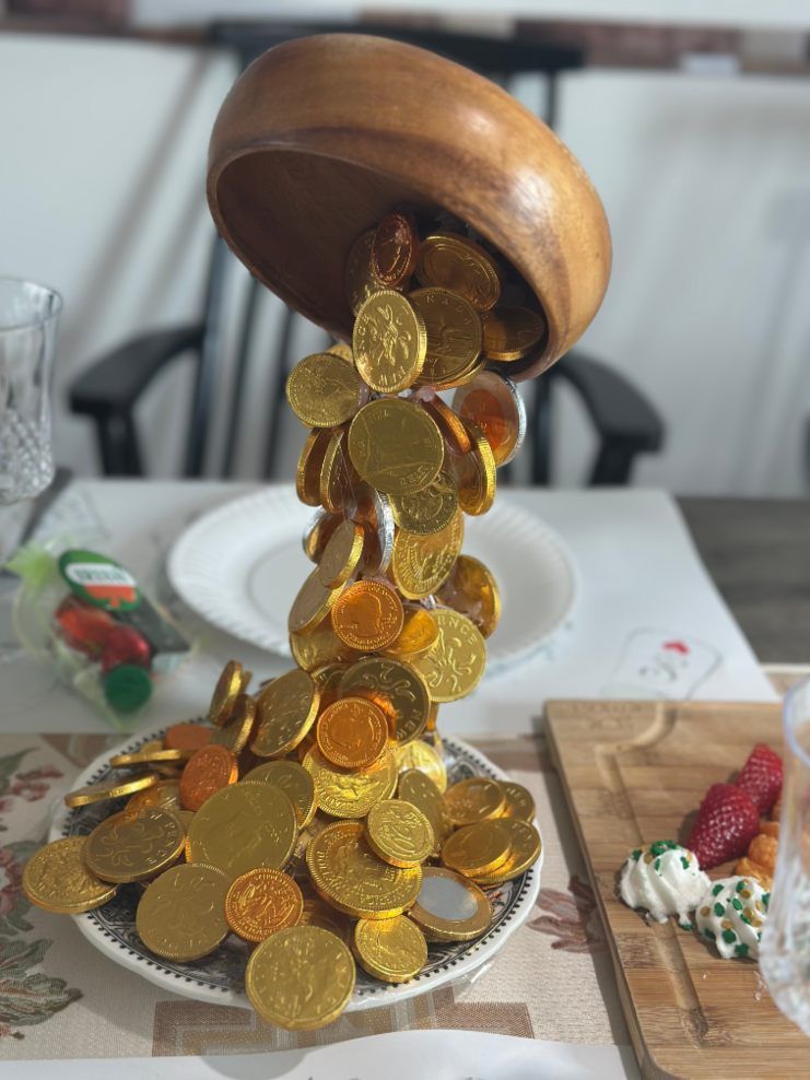 A wooden bowl appears to pour gold coins onto a plate. Coins also scattered around the base.