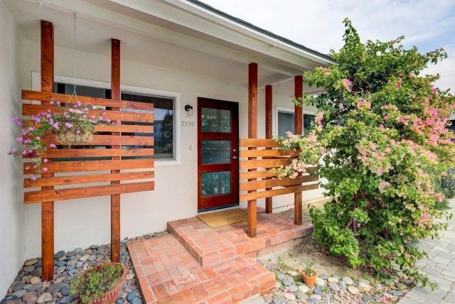 Mid-century home exterior with wooden details, door, and flowering shrub.