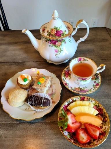 Tea set with teapot, teacup, pastries, and fruit on a wooden table.