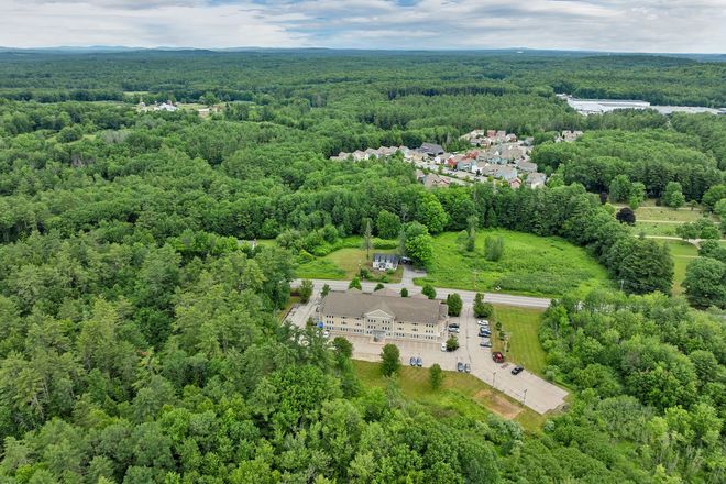 Aerial view of a house and parking lot surrounded by dense green forest under a cloudy sky