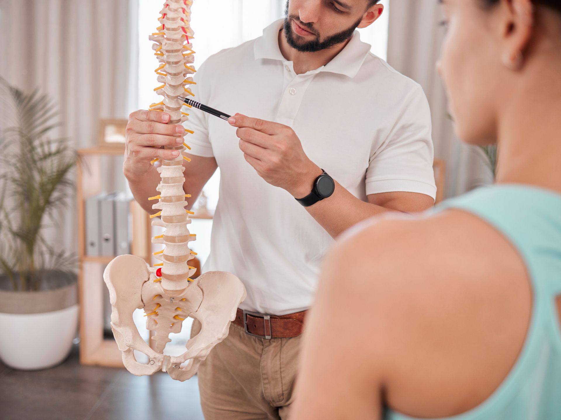 A man is holding a model of a spine and talking to a woman. WellLife Chiropractic
