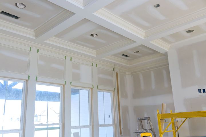 Interior of a room under construction, with drywall on walls and ceiling, window, and unfinished floor.