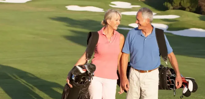 A man and a woman are walking on a golf course holding golf bags.