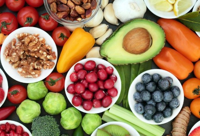 A variety of fruits and vegetables in bowls on a table.