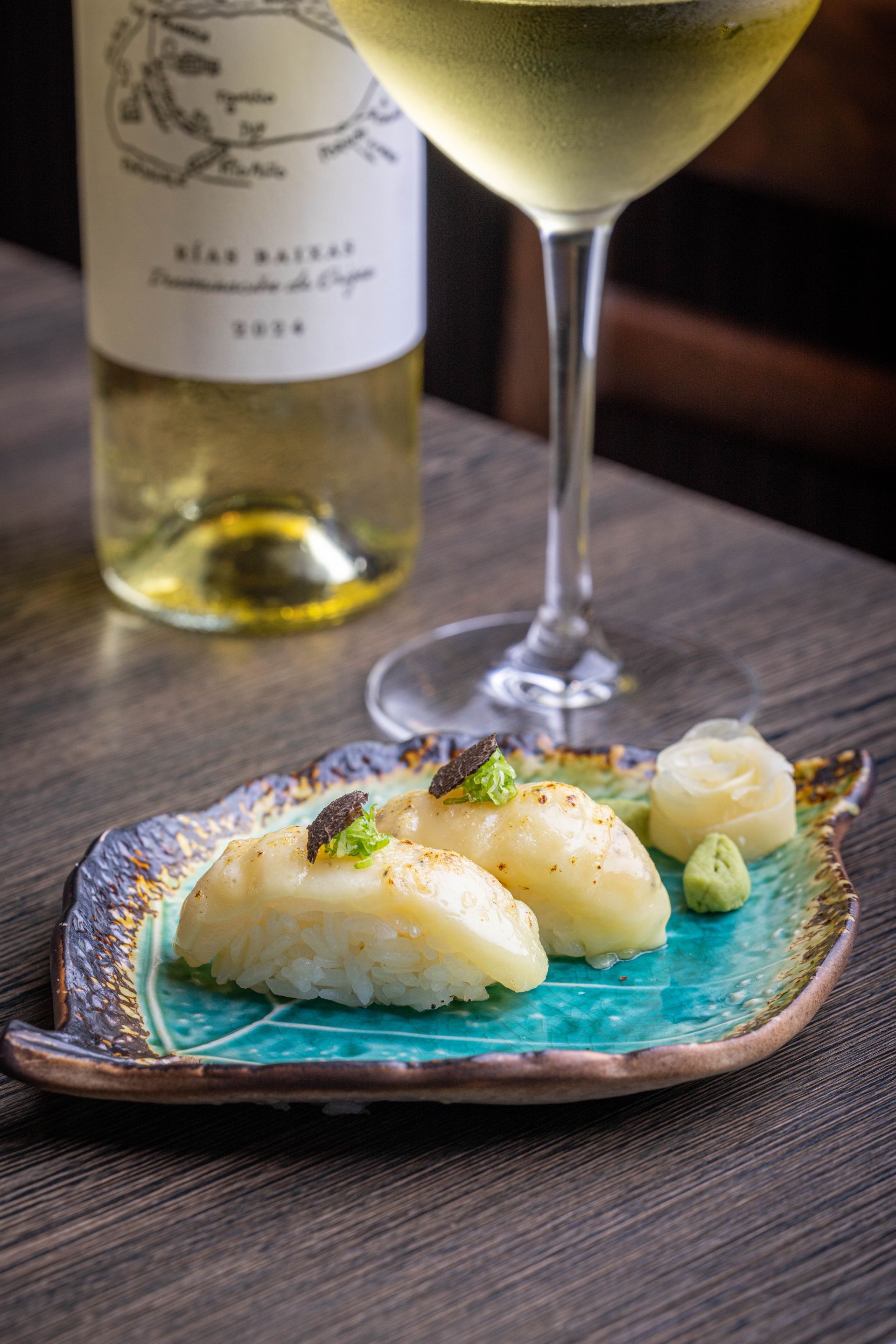 White fish dish on a turquoise plate beside a wine glass and bottle on a table
