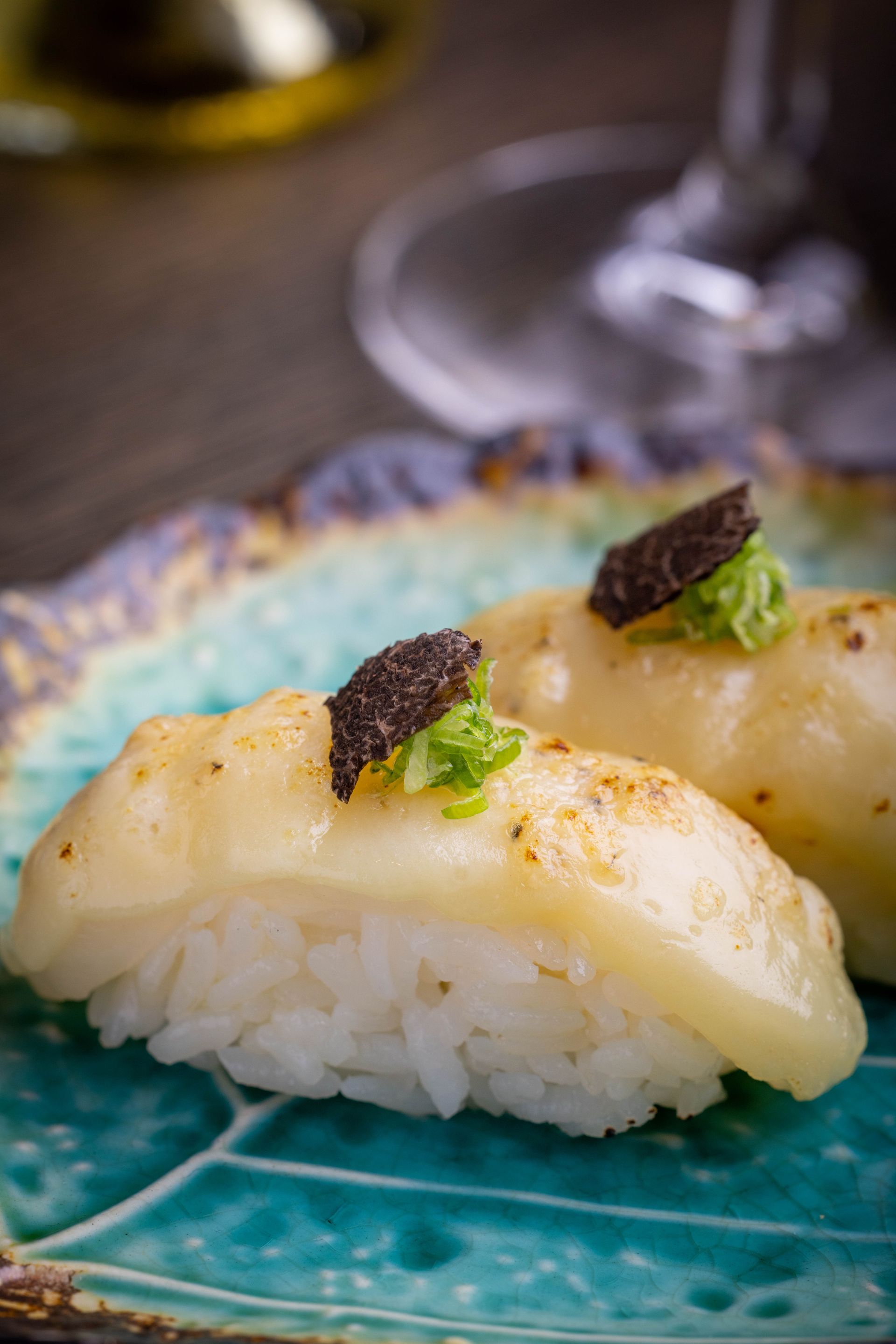 Sushi nigiri topped with seared scallops, green garnish, and black caviar on a blue plate