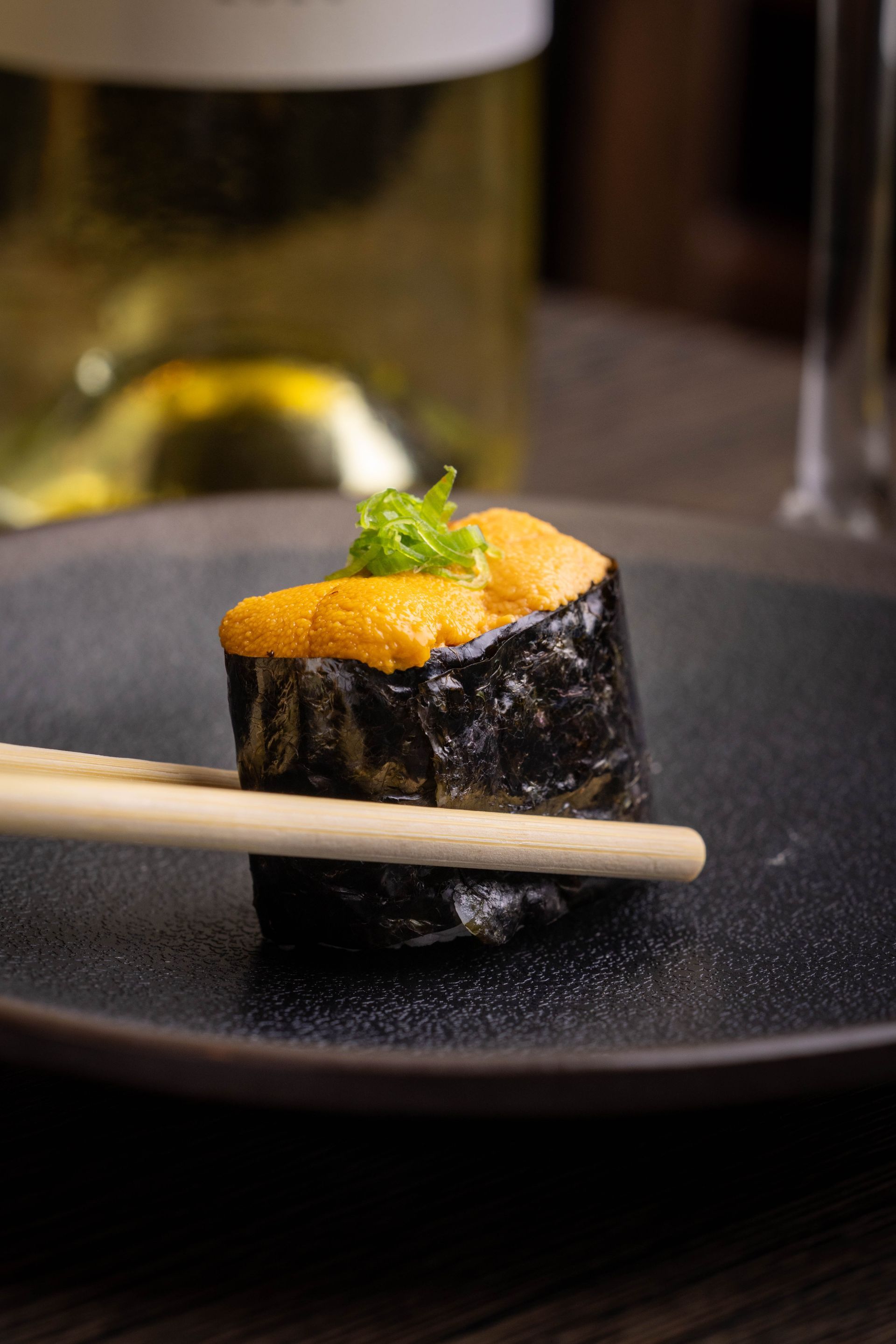Sushi roll with orange topping and herb garnish on a black plate with chopsticks