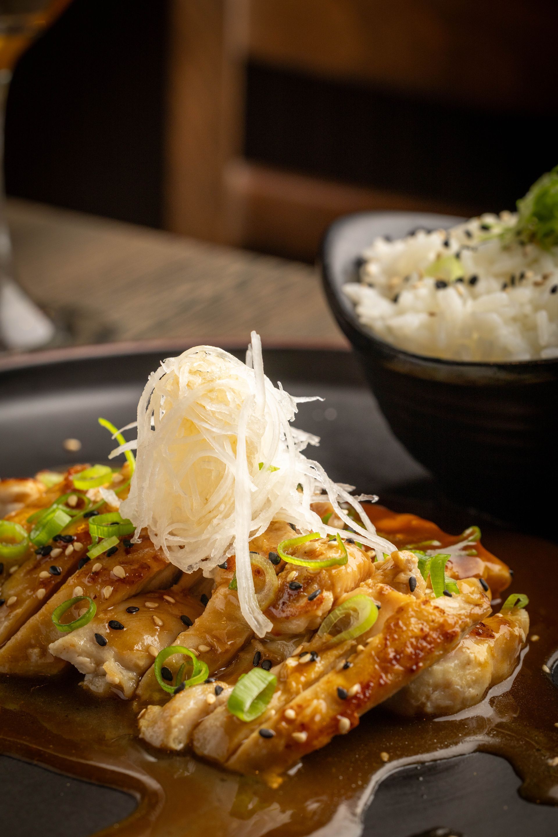 Glazed grilled fish topped with shredded daikon on a plate, with a bowl of rice in the background