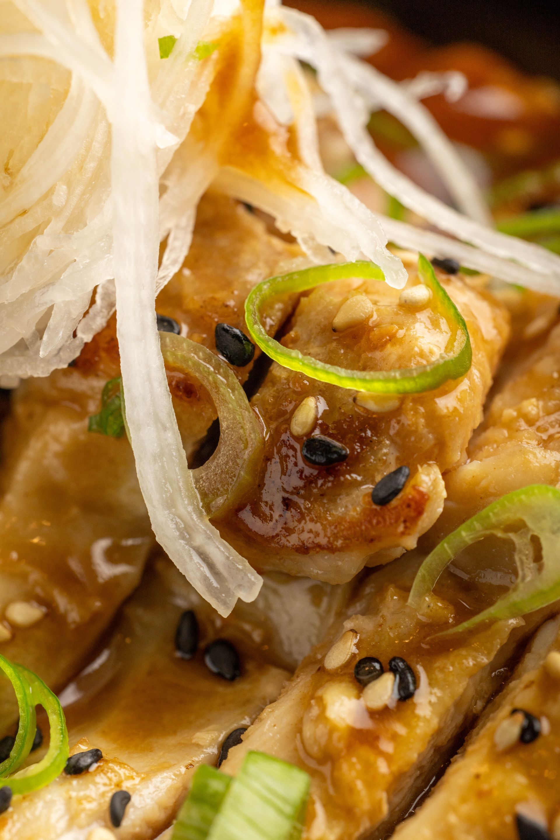 Close-up of glazed grilled chicken with black sesame seeds and sliced green onions