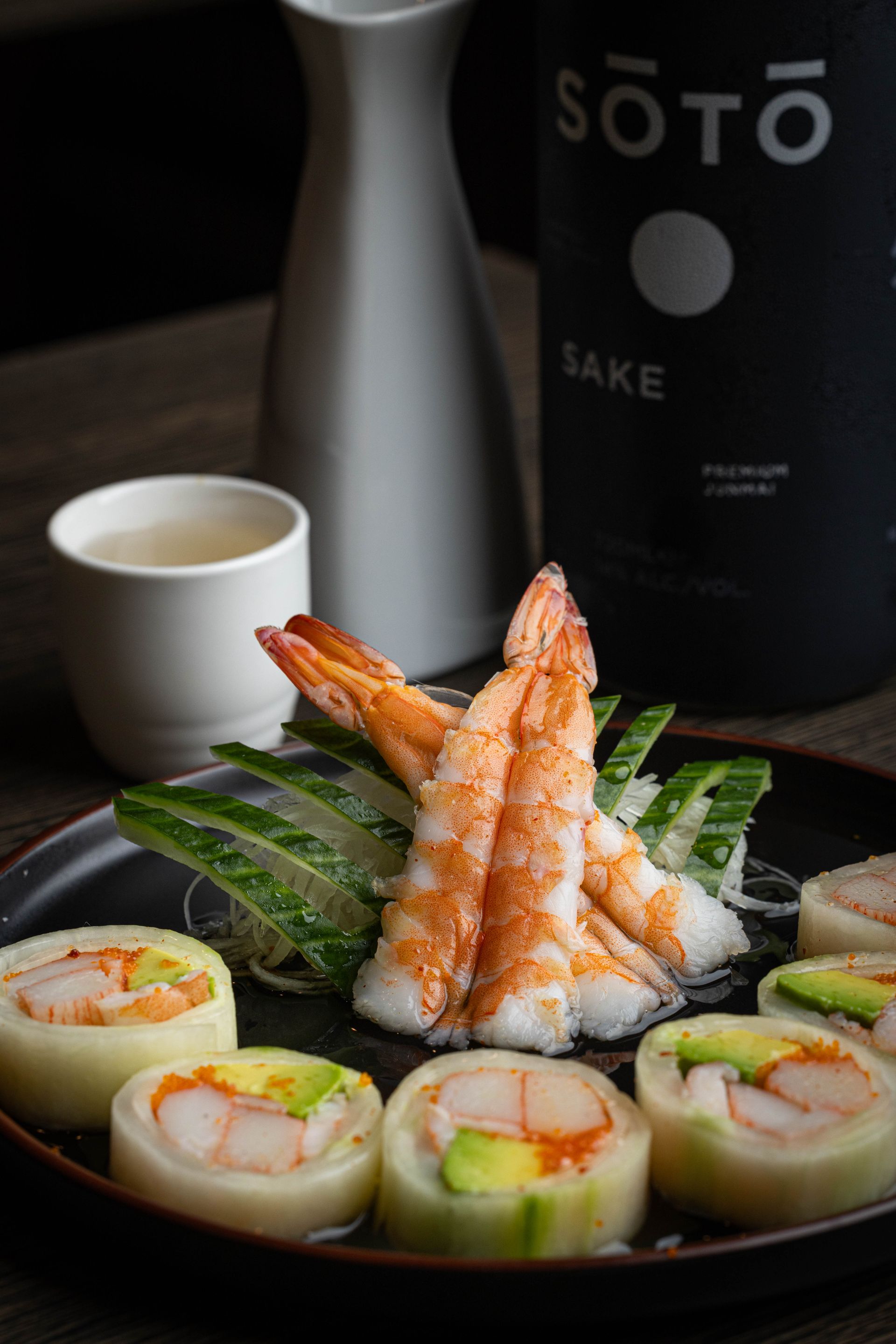 Sushi platter with shrimp nigiri, maki rolls, dipping sauce, and a bottle of Sōtō sake