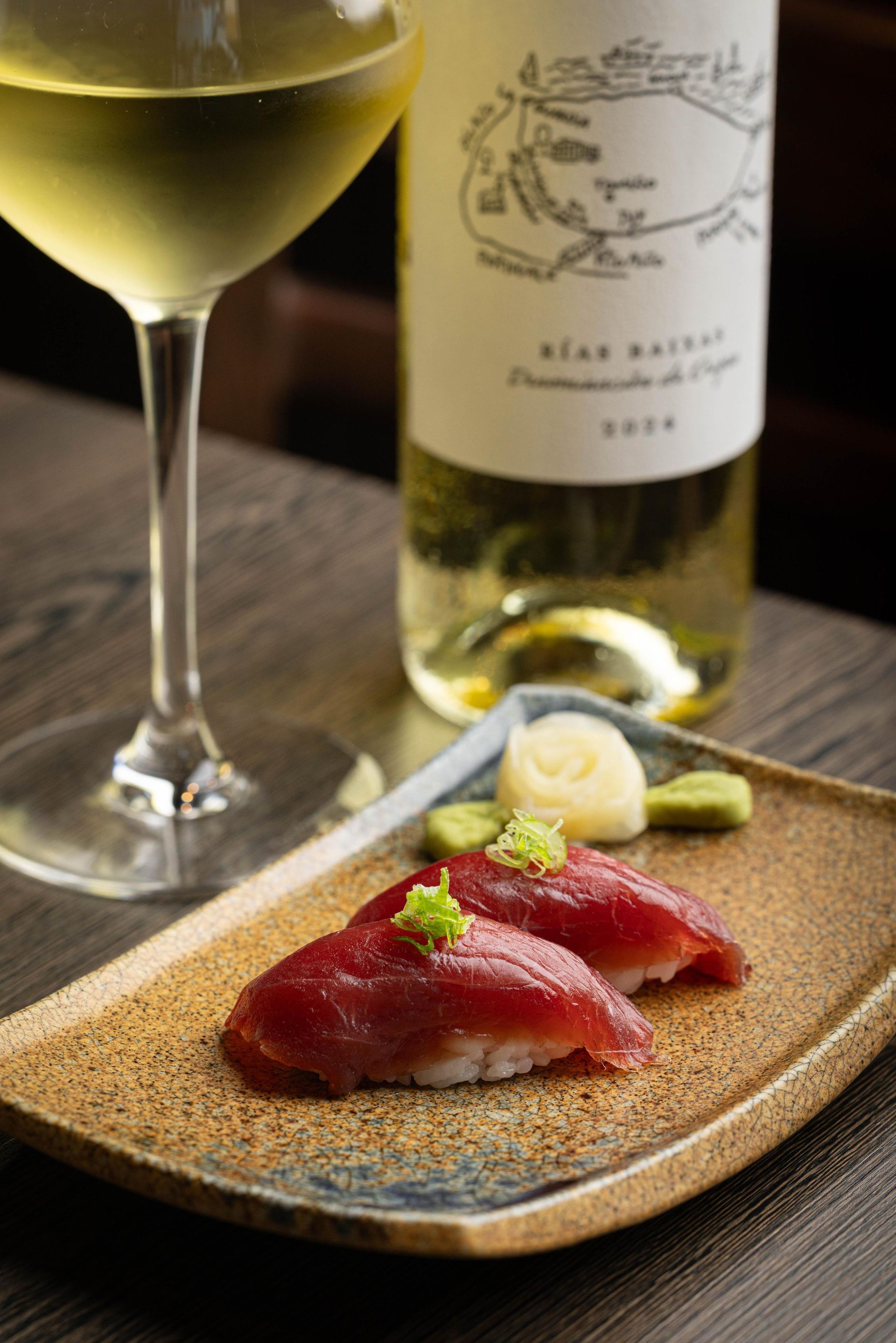 Seared tuna slices on a plate with a lemon rose, beside a wine glass and bottle