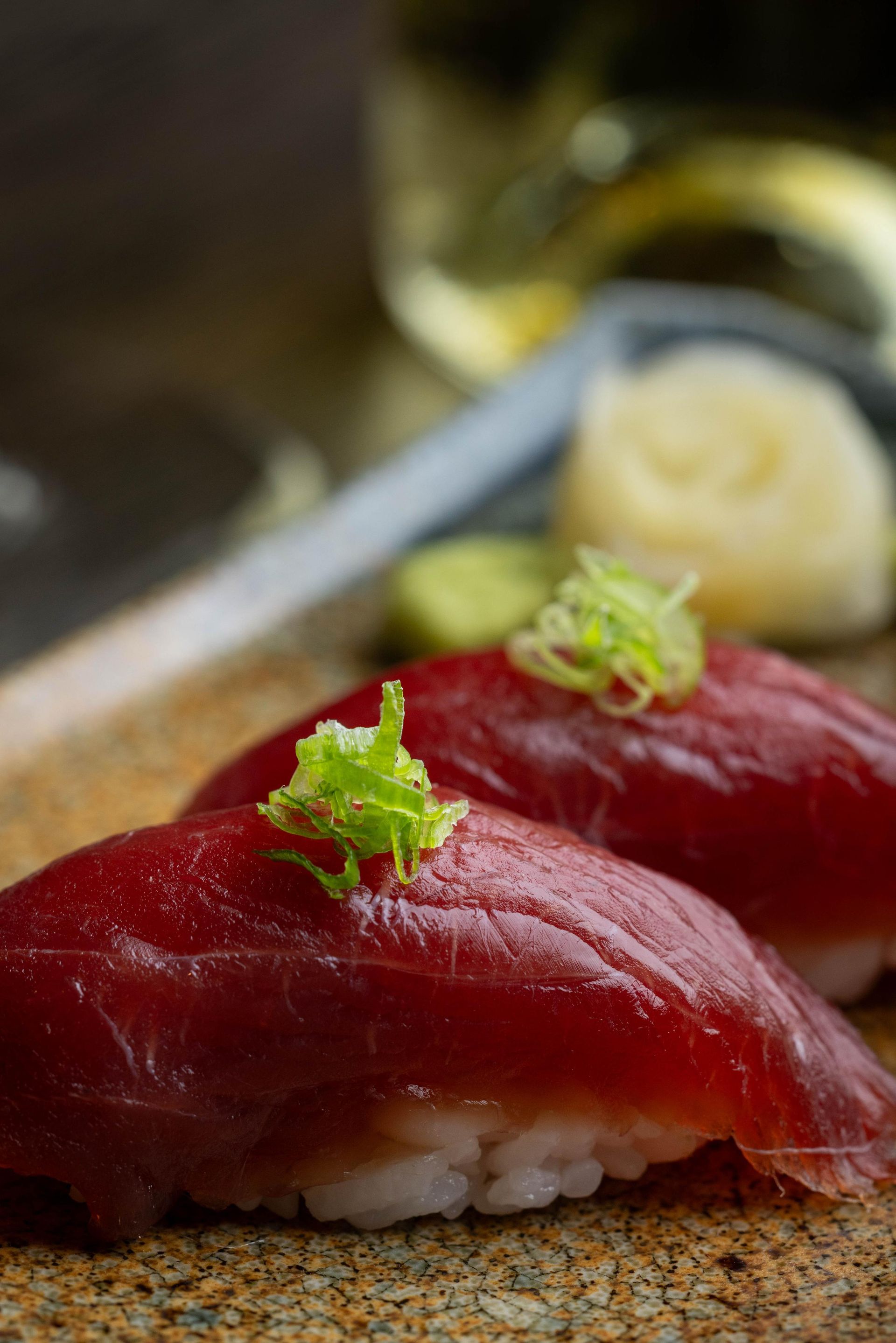Red tuna sushi nigiri topped with green garnish on a plate with wasabi and pickled ginger.