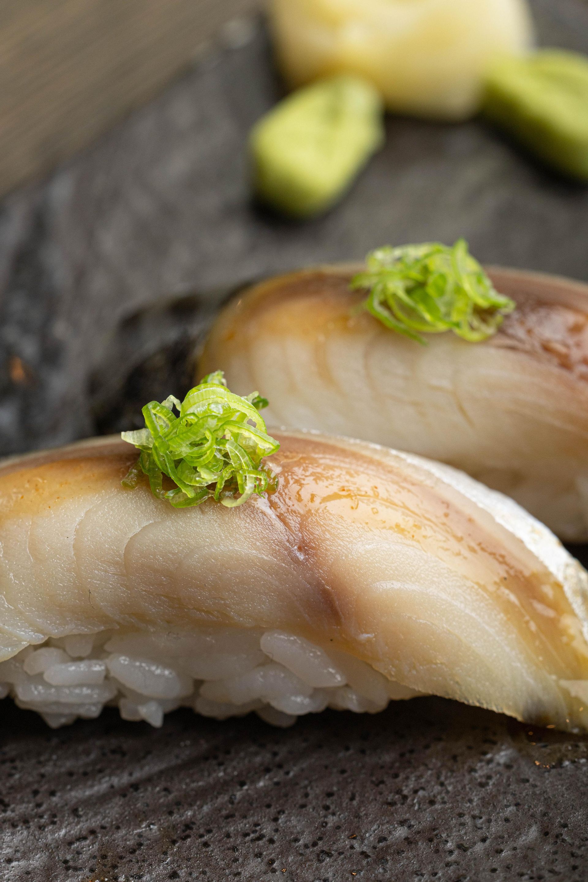 Close-up of two pieces of nigiri sushi topped with green garnish on a dark plate