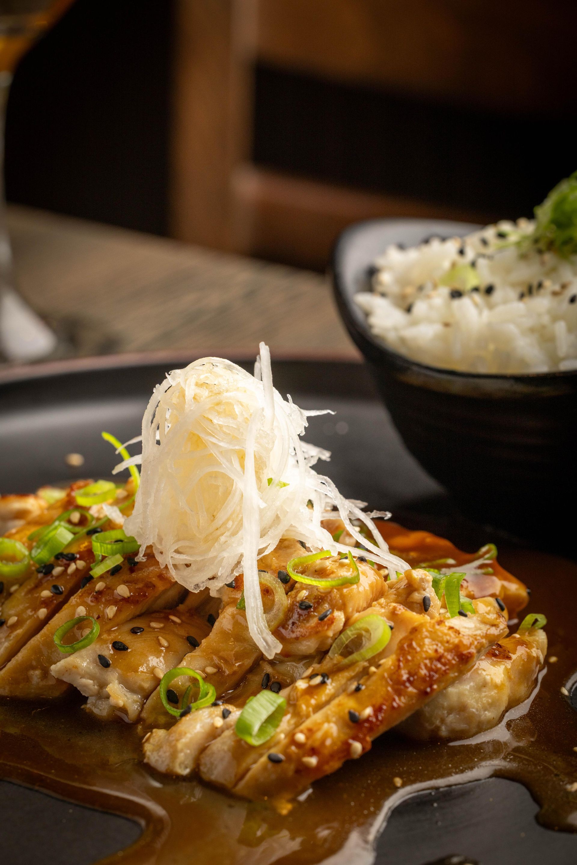 Grilled fish topped with shredded garnish and green onions beside a bowl of rice