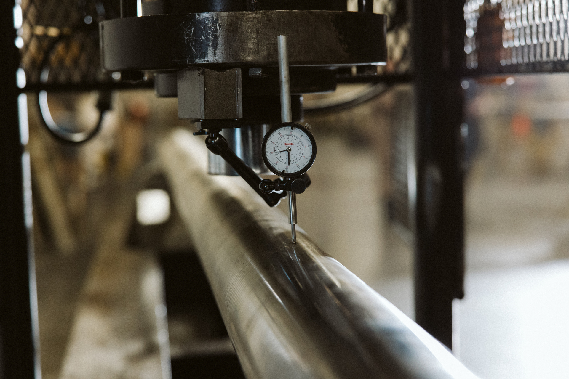 Close-up of a dial indicator measuring a metal rod's alignment within machinery, in an industrial setting.