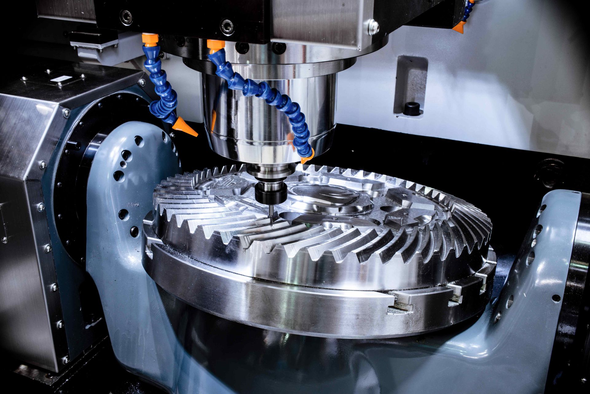 CNC machine cutting teeth into a large, metallic gear. Coolant sprays as it works.