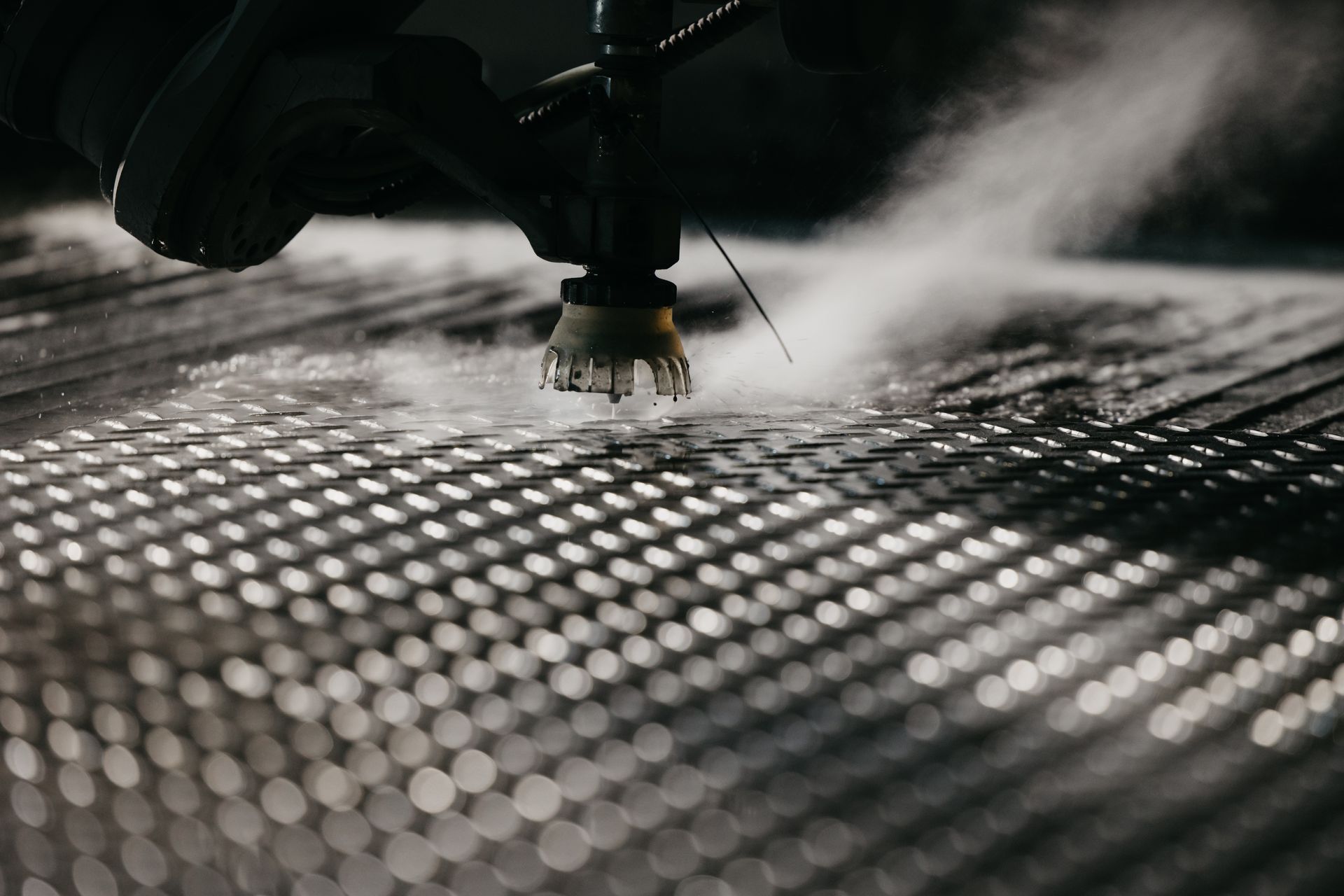 Water jet cutting a metal sheet, creating steam.