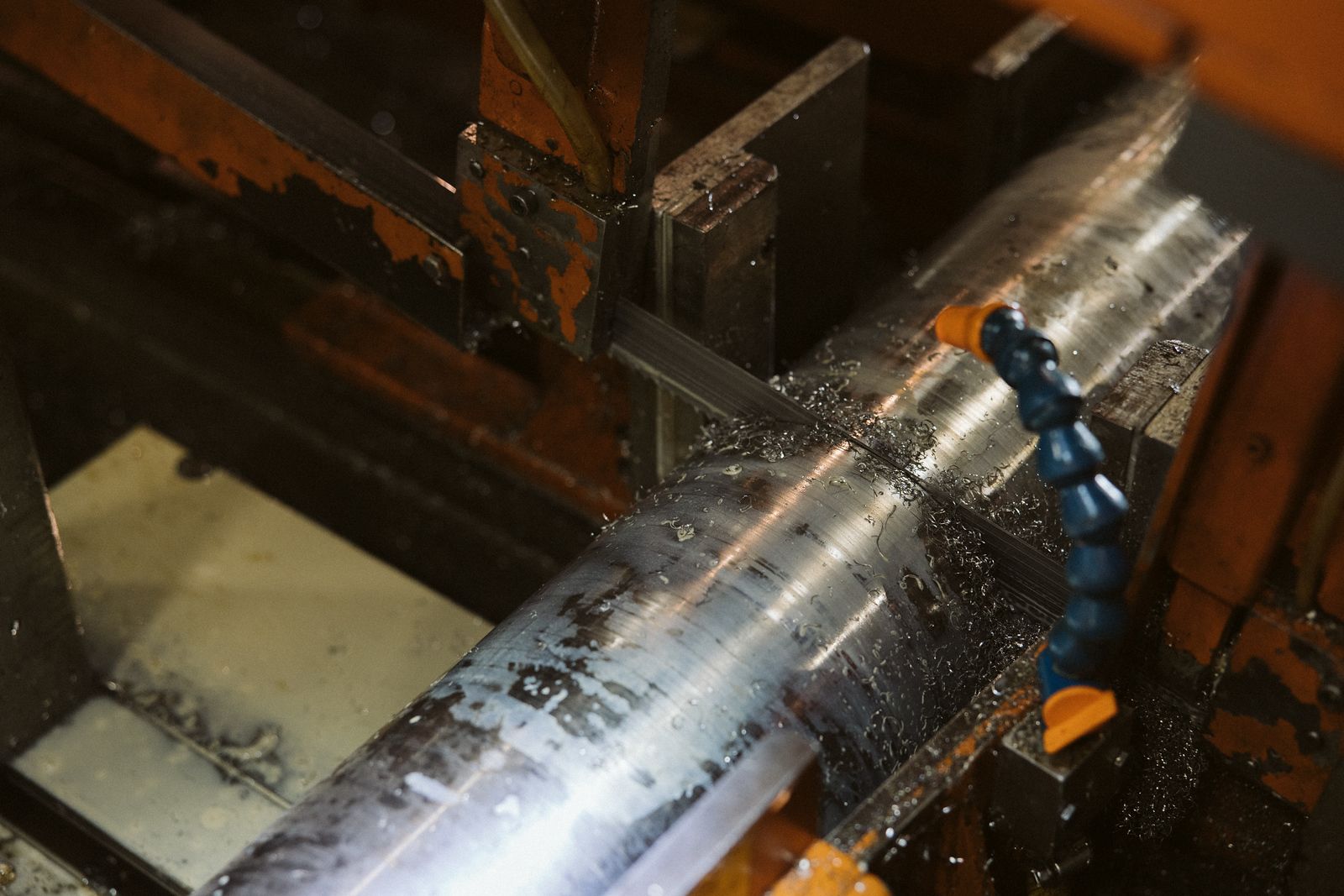Metal rod being cut by a bandsaw with coolant spraying, in a workshop setting.