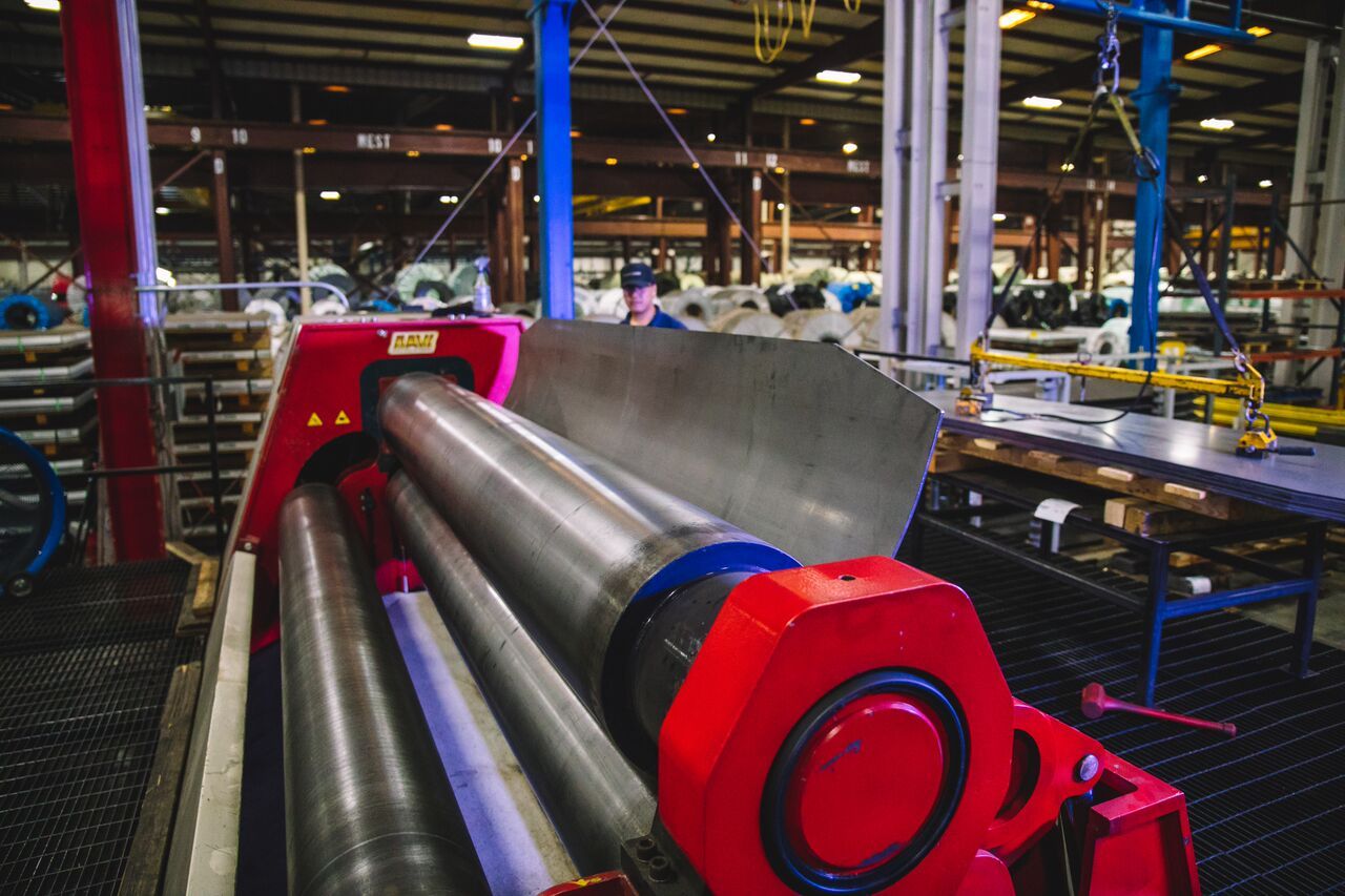 Metal roller machine in a factory, with a person operating it. Red, gray and blue machine.