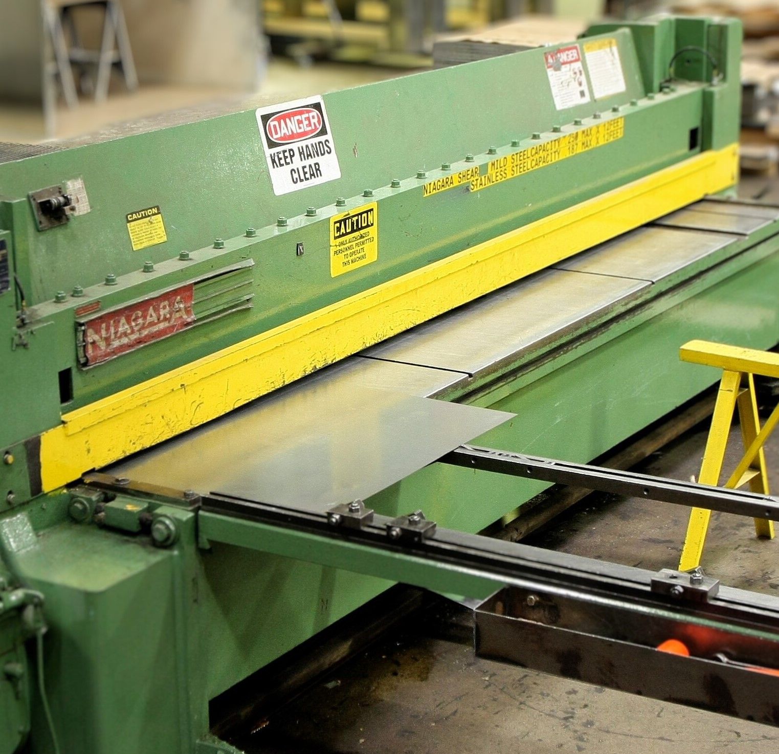 Green industrial shear machine cutting a metal sheet in a factory setting.