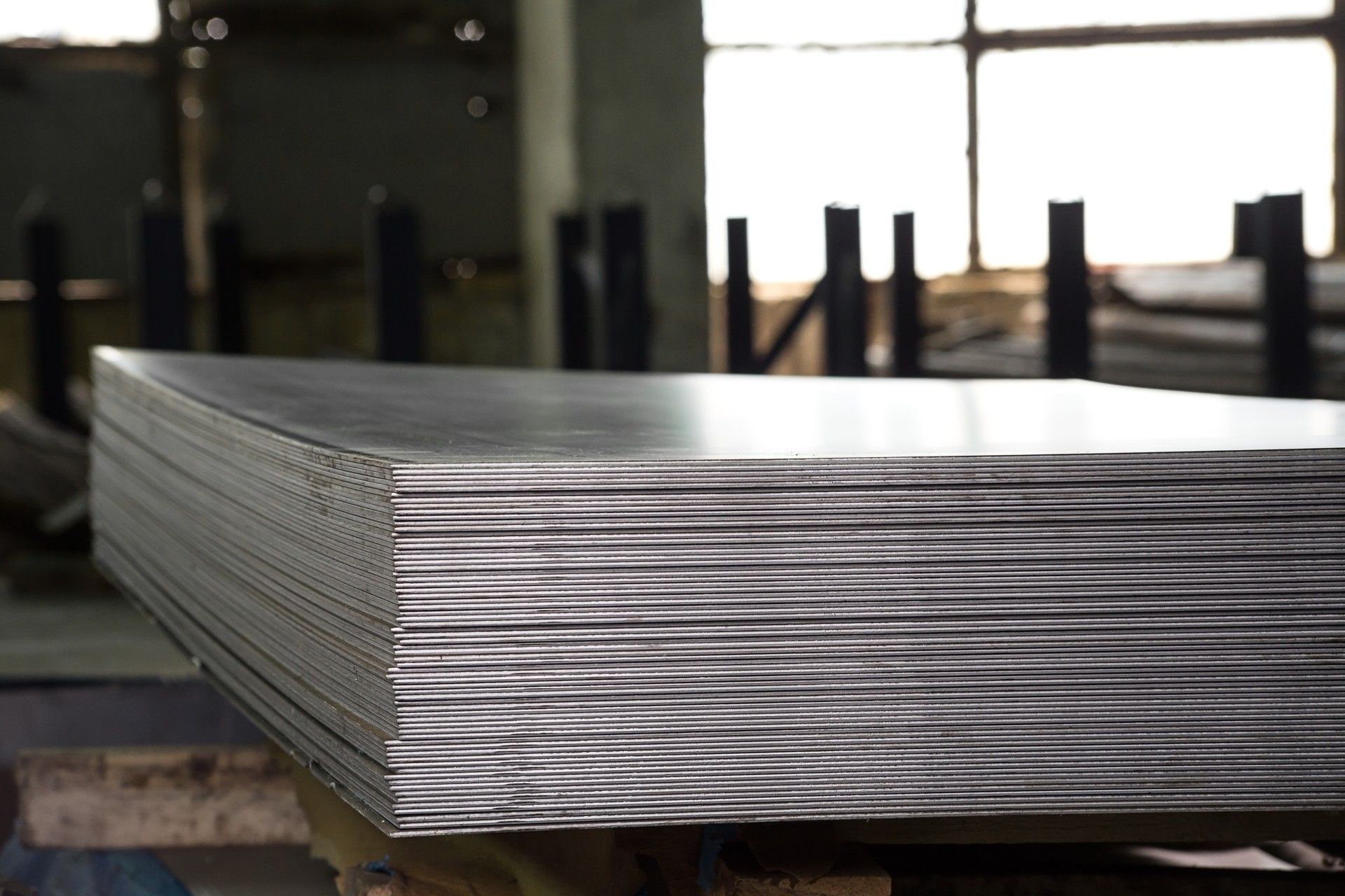 Stack of metal sheets in a warehouse, reflecting light.