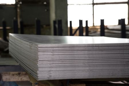 Stack of metal sheets in a warehouse, reflecting light.