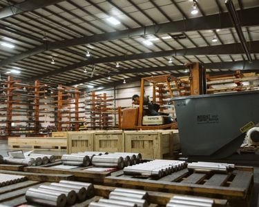 Warehouse interior with forklift, metal cylinders, wooden crates, and shelving.