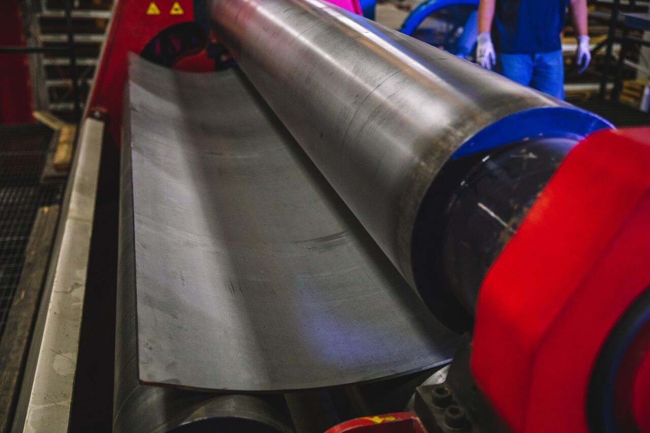 Metal sheet being rolled into a curved shape by a large machine with red and silver components.
