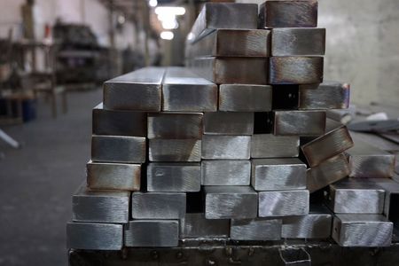 Stack of rectangular metal bars in an industrial setting, with visible cut ends and a reflective surface.