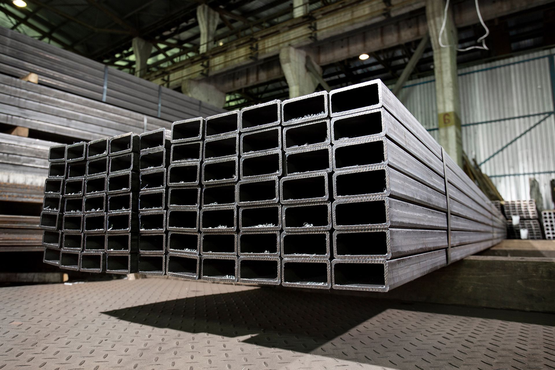 Stacks of rectangular steel tubes in a warehouse setting.