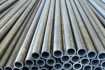 Piles of gray metal tubes with hollow openings, stacked together in a storage area.