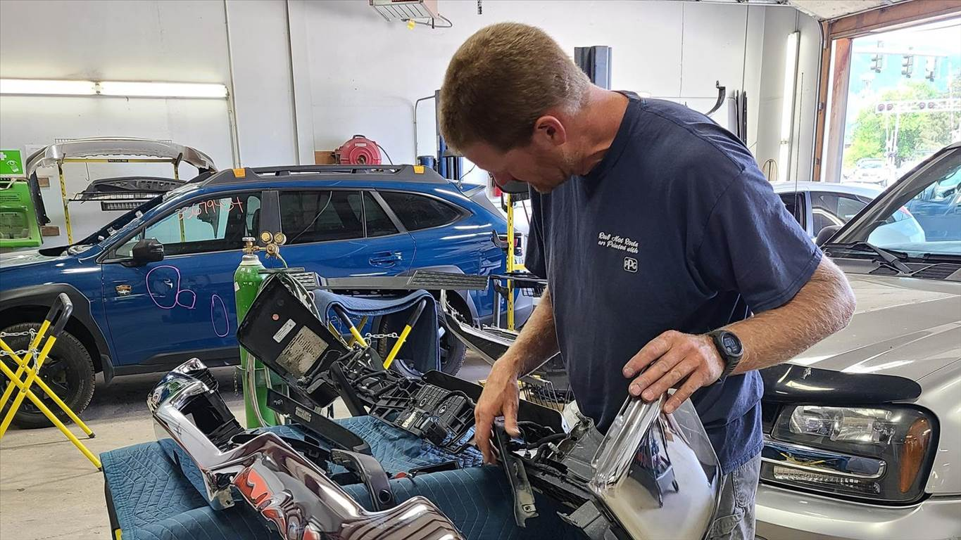 Dave Fox examines car parts inside a garage with a blue SUV in the background.