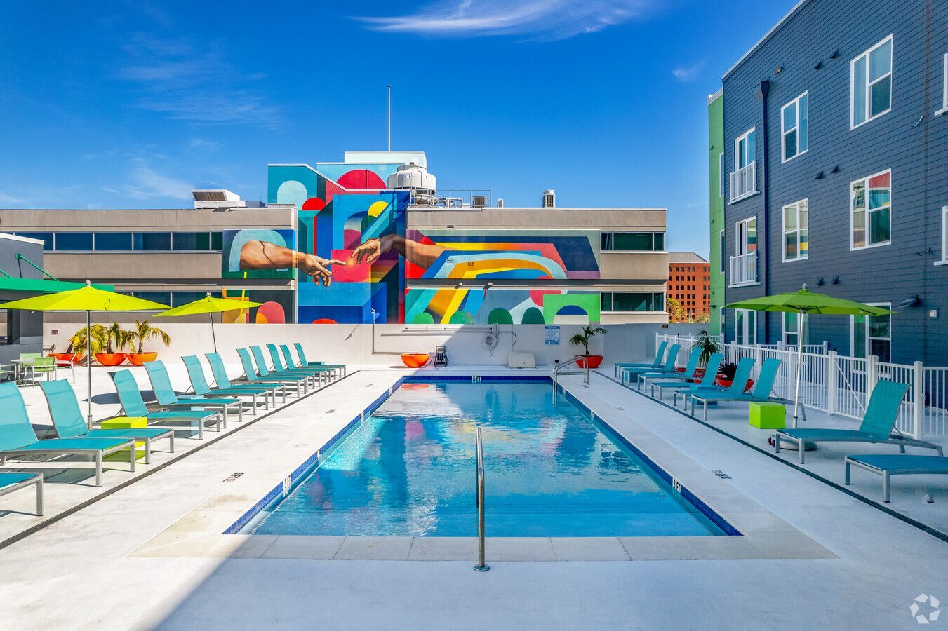 A large swimming pool surrounded by chairs and umbrellas in front of a building.