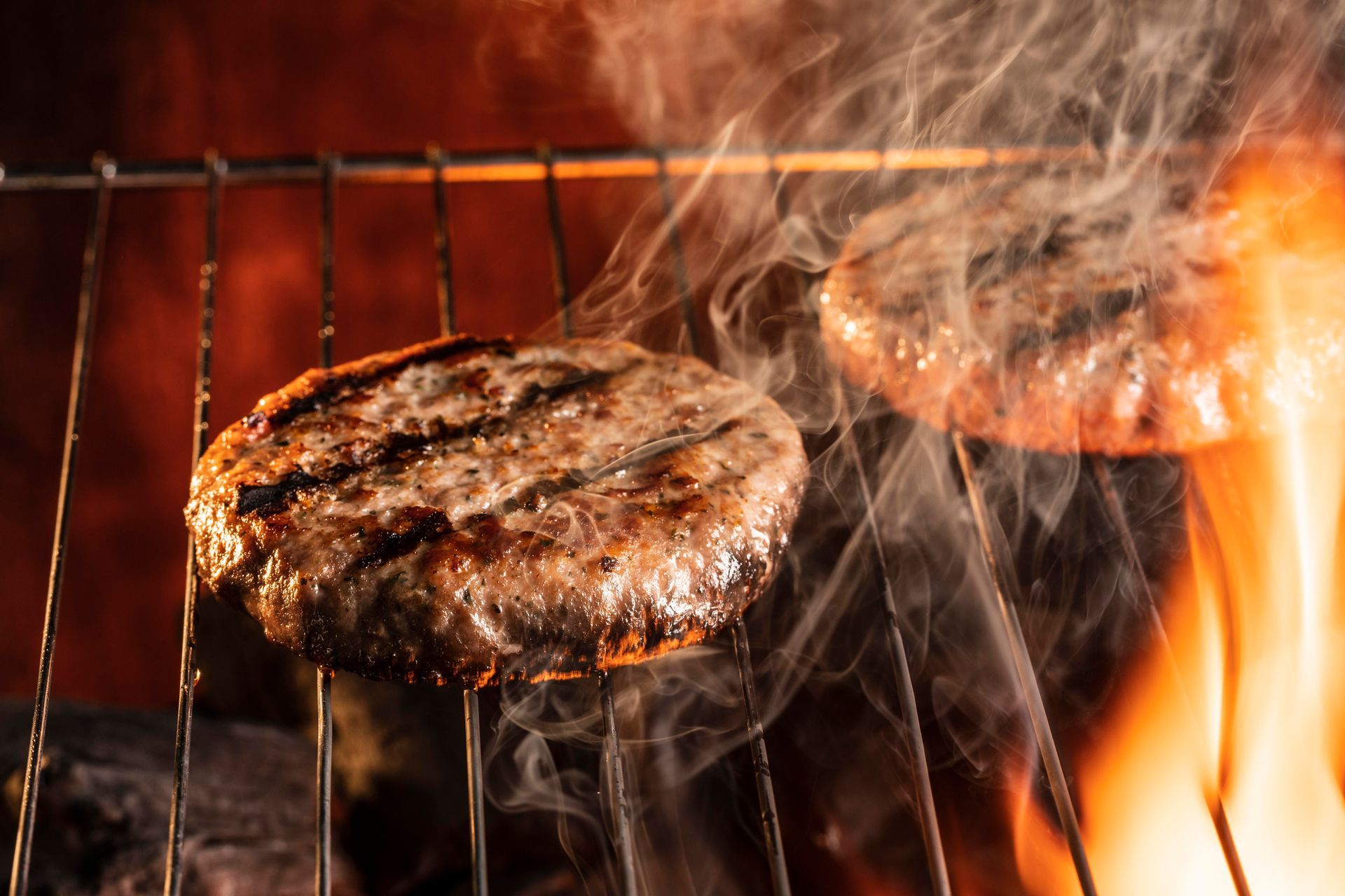 Two hamburgers are cooking on a grill over a fire.