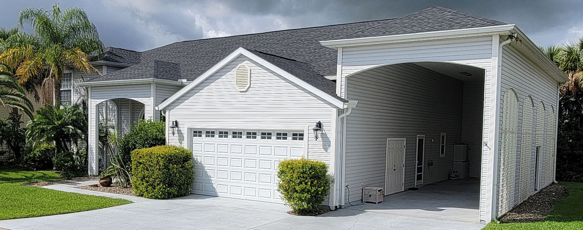 White suburban house with a two-car garage, arched carport, and palm trees in the front yard