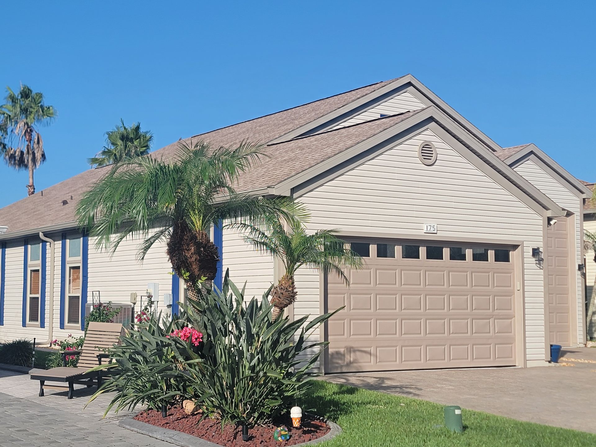 Single-story beige house with a tan garage, palm trees, and desert landscaping under a clear blue sky