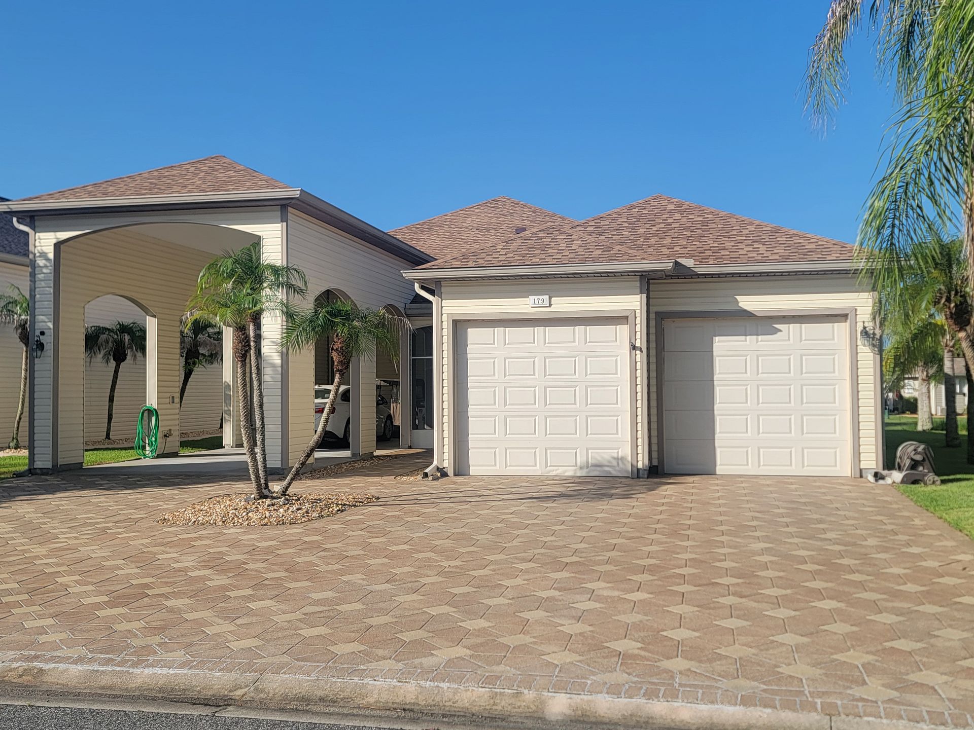 Single-story house with a tiled roof, double garage, and a brick-paved driveway under a blue sky