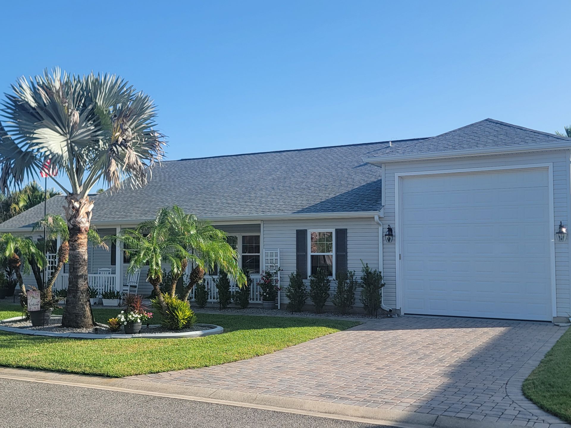 Single-story house with a tiled roof, palm trees, and a white garage door under a clear blue sky