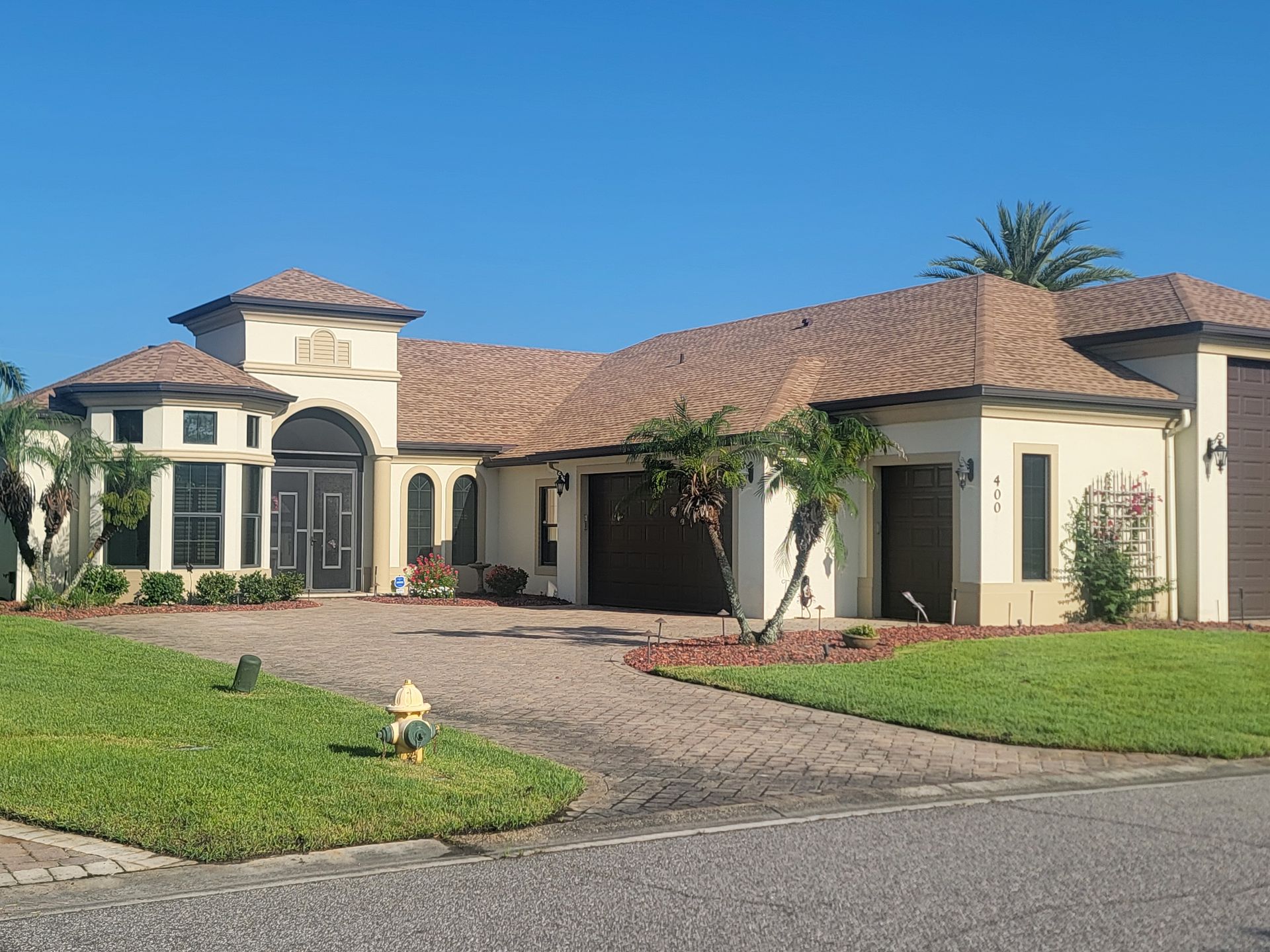Single-story stucco house with a tiled roof, arched entry, and landscaped front yard under a blue sky