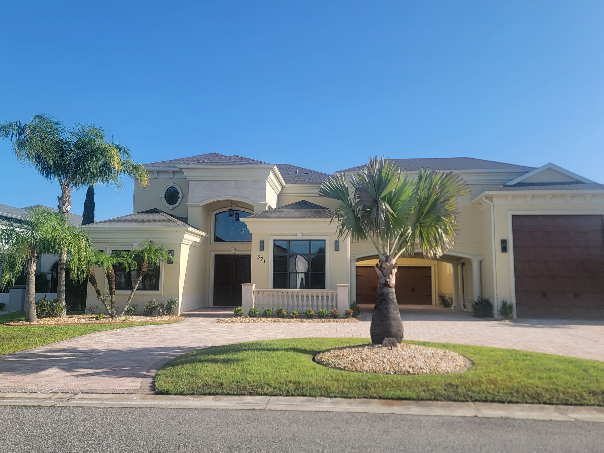 Suburban house with a beige stucco exterior, palm trees, and a two-car garage under a clear blue sky