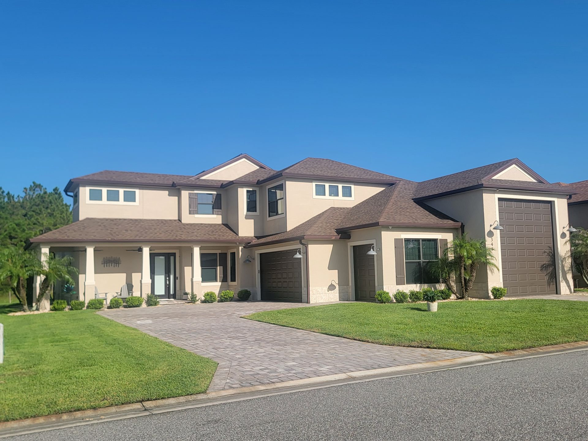 Large beige suburban house with a tiled roof, driveway, and green lawn under a clear blue sky