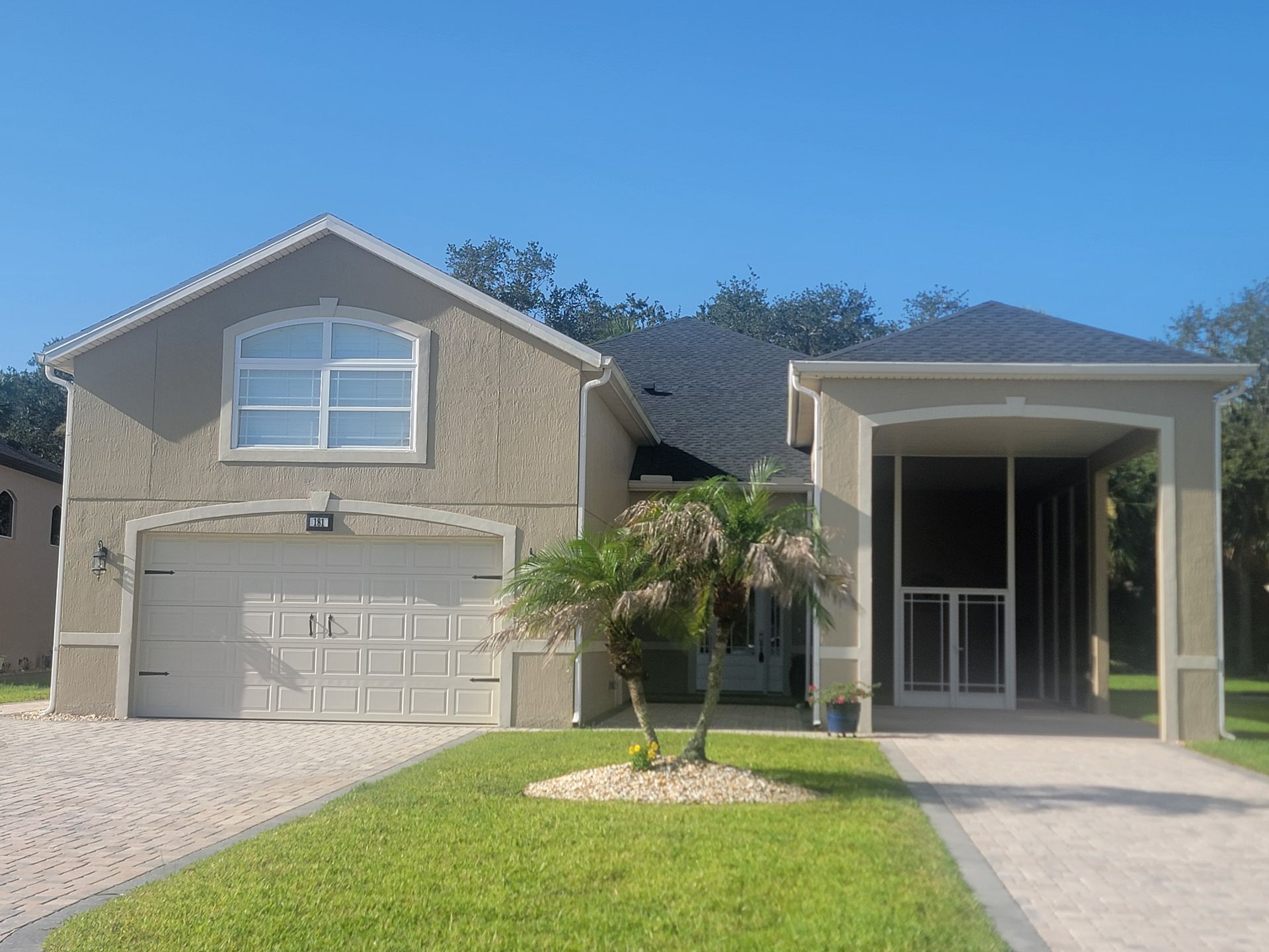 Suburban two-story house with a garage, front palm tree, and a covered entry walkway under a clear blue sky