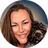 Smiling woman with blonde hair posing with a small black dog against a blue background