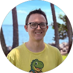 Smiling person in glasses and a yellow shirt outdoors with ocean and palm trees in the background