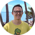 Smiling person in glasses and a yellow shirt outdoors with ocean and palm trees in the background