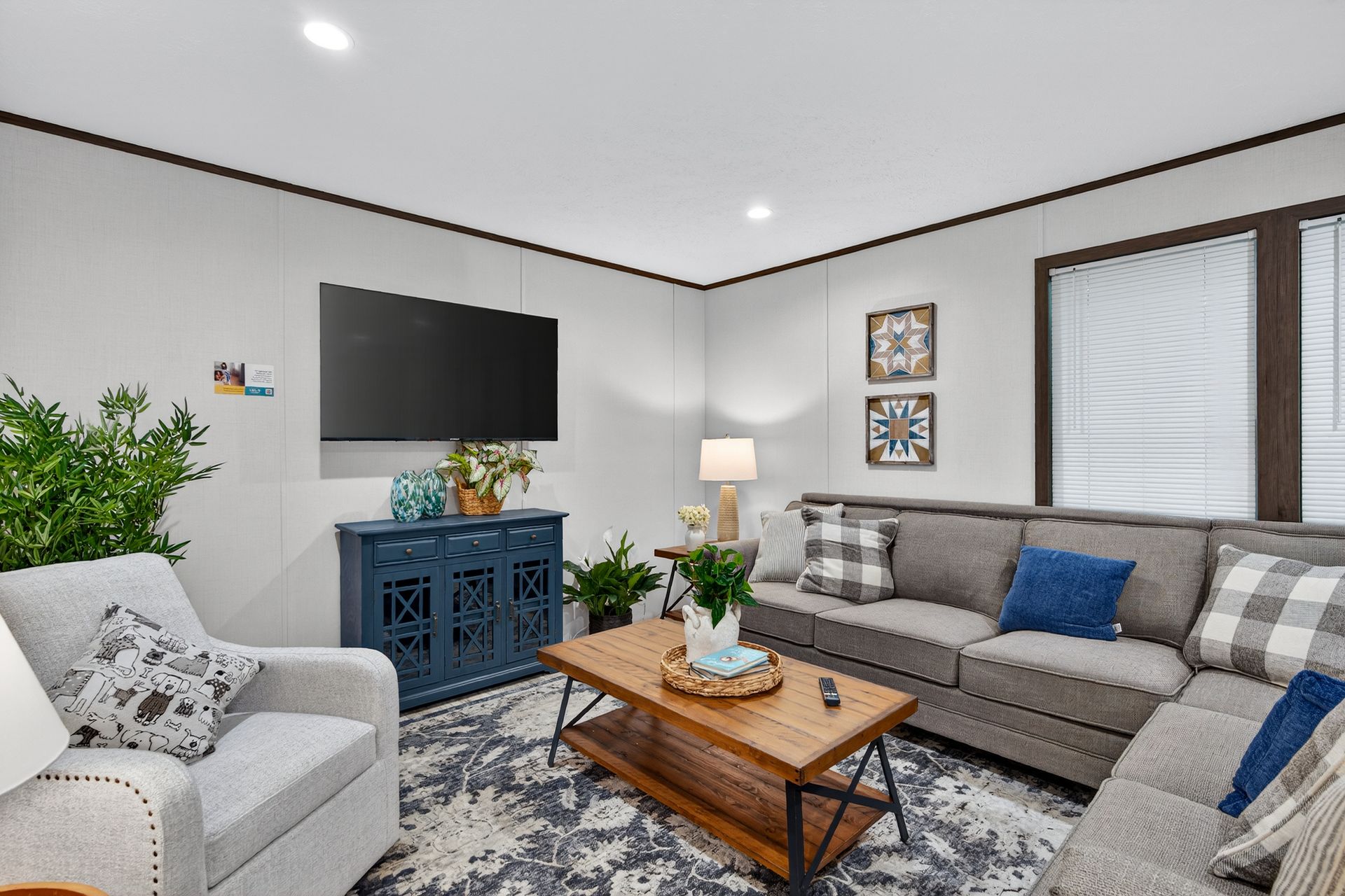 Bright living room with gray sofas, TV on blue console, wooden coffee table, and window curtains